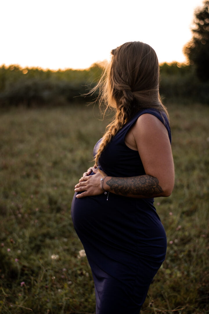 photo d'une femme qui touche son ventre à la fin de sa grossesse dans un champ lors d'un coucher de soleil près de rennes