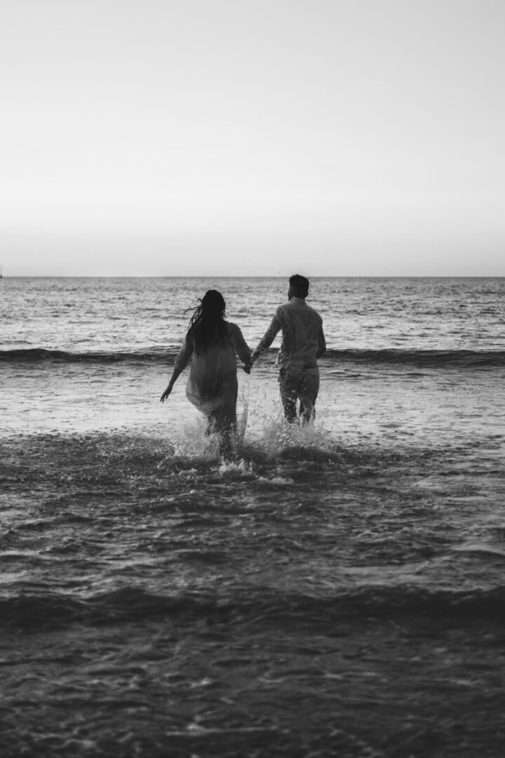 Couple se tenant la main dans l'eau lors d'un shooting engagement à la plage